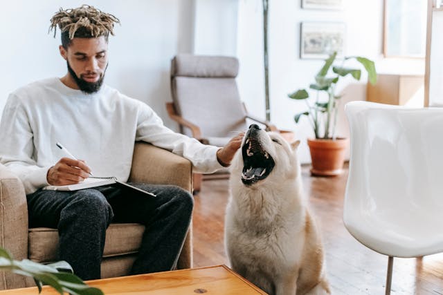 A person caressing his dog while taking notes.