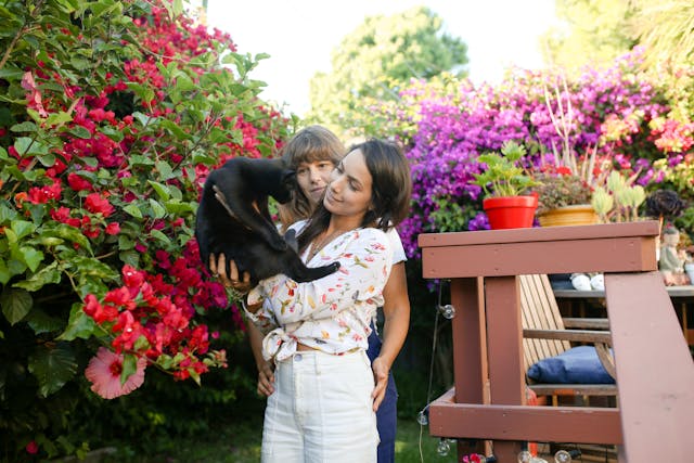 A woman standing in her house lawn lifting a black cat.